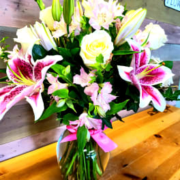 Bouquet of pink lilies, white roses, and pale pink flowers in a glass vase