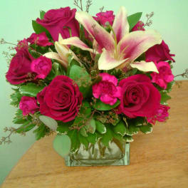 Pink roses and lilies arranged in a square glass vase