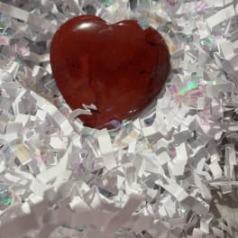 Red polished heart-shaped stone nestled in white crinkle paper filling