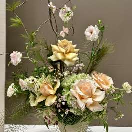 Tall floral arrangement with peach roses, pale blooms, and branching stems in a vase