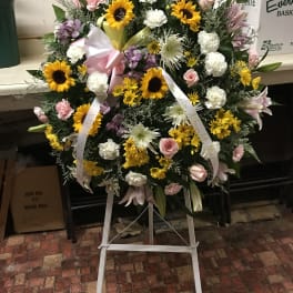 Large standing floral wreath with sunflowers, pink roses, and white blooms on an easel