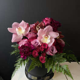 Pink orchids and roses arranged in a black hat box