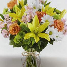 Bouquet of orange roses, yellow lilies, and white daisies in a glass vase