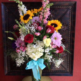 Mixed bouquet in a glass vase with sunflowers, roses, and daisies