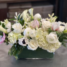 White floral arrangement with roses, ranunculus, and calla lilies in a green vase