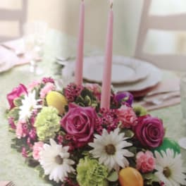 Pink floral centerpiece with two tall candles on a table