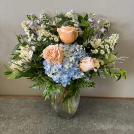 Mixed bouquet of peach roses, blue hydrangea, and small white daisies in a glass vase