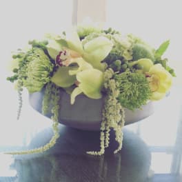 Green floral arrangement with orchids and cascading greenery in a bowl vase