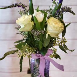 White roses and tulips in a purple glass vase with a lavender ribbon