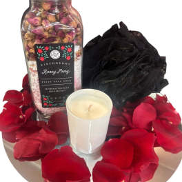 Rose petals with a bath soak jar, candle, and black bath pouf on a tray