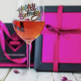 Wine glass with a colorful happy birthday decal, filled with pink drink