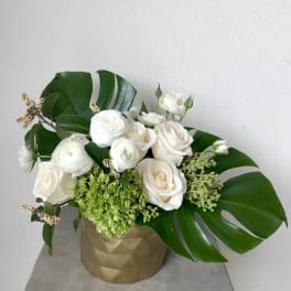 White roses and ranunculus in a gold vase with large tropical leaves