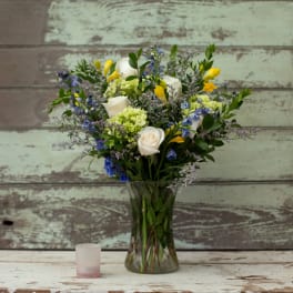 Bouquet of white roses, yellow blooms, and blue flowers in a glass vase