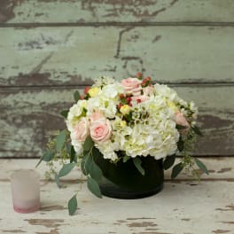 Pink roses and white hydrangeas in a dark vase with a small candle beside it