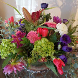 Mixed bouquet with pink, purple, white, and green flowers in a low container