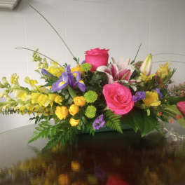 Colorful mixed flower arrangement with roses, lilies, and snapdragons in a low container