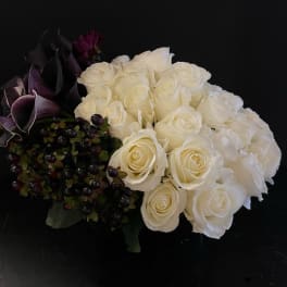 Low arrangement of white roses with dark purple calla lilies and berries.
