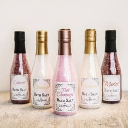 Five labeled bottles of bath salt in pink, gold, and white tones