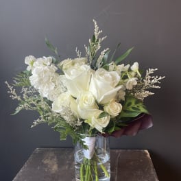 White rose bouquet in a clear glass vase with mixed greenery