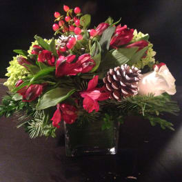 Red and white floral arrangement in a square glass vase with a pinecone accent