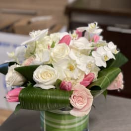 White and pink bouquet in a glass vase with broad green leaves
