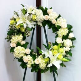 White floral wreath with lilies, roses, and hydrangeas on an easel