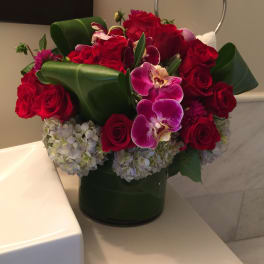 Bouquet of red roses, purple orchids, and pale hydrangeas in a green vase