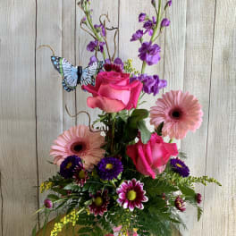Pink roses and gerbera daisies in a decorated vase with a butterfly accent