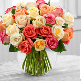 Mixed roses in peach, pink, cream, and yellow in a clear glass vase