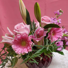 Pink bouquet with gerbera daisies, roses, lilies, and purple flowers in a faceted vase