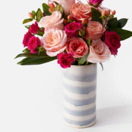 Pink and coral roses arranged in a striped ceramic vase