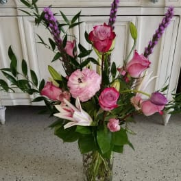 Pink roses and lilies in a clear glass vase with purple spikes