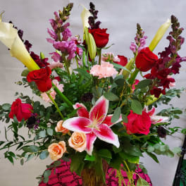 Tall mixed bouquet with red roses, pink lilies, and calla lilies in a glass vase