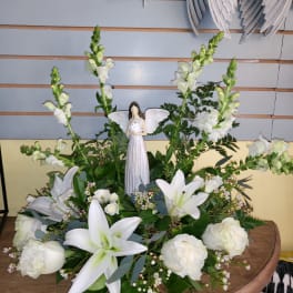 White floral arrangement with lilies and roses topped by an angel figurine