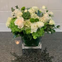 White and green floral arrangement in a square glass vase