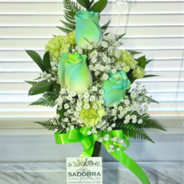 Tall vase arrangement with green-tinted roses, light carnations, baby's breath, and a bright green ribbon bow