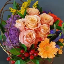 Colorful arrangement of peach roses, orange gerbera, and mixed blooms in a low container