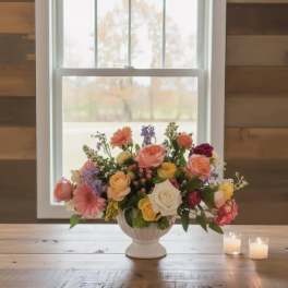 Mixed pastel flower arrangement in a white vase on a wooden table