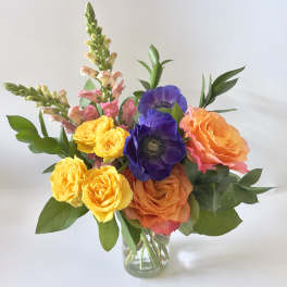 Colorful bouquet of roses and purple anemones in a glass vase