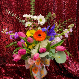 Bright mixed bouquet with pink tulips, daisies, iris and gerbera in a glass vase with a floral bow.