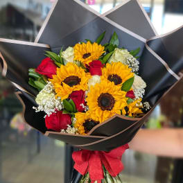 Bouquet of sunflowers and red roses wrapped in black paper with a red bow