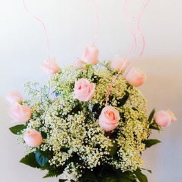 Pink roses in a glass vase with baby's breath and pink curly picks