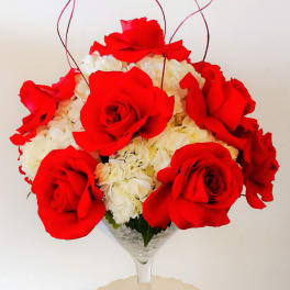 Red roses and white hydrangeas in a wine glass vase with curly red accents