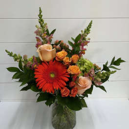 Mixed bouquet with orange gerbera daisies and peach roses in a glass vase