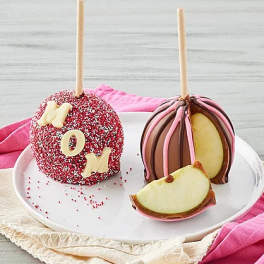 Two chocolate-covered caramel apples on sticks, one with sprinkles and letters