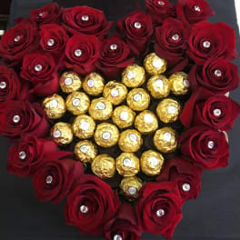 Heart-shaped arrangement of red roses surrounding gold-wrapped chocolates