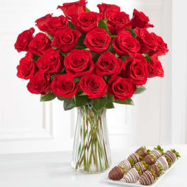 Red roses in a clear glass vase with chocolate-covered strawberries on a tray