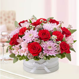 Red roses and pink chrysanthemums in a white hat box with a ribbon