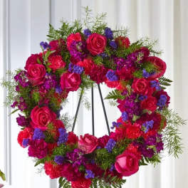 Circular floral wreath with pink roses, red carnations, and purple filler flowers