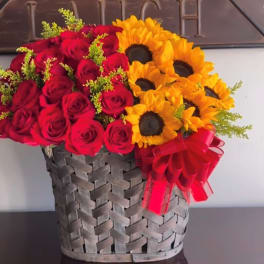 Red roses and yellow sunflowers arranged in a woven basket with a red ribbon